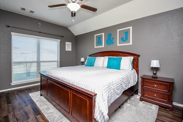 bedroom featuring dark wood-style floors, visible vents, lofted ceiling, and a textured wall