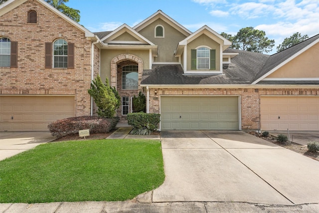 traditional-style house with stucco siding, driveway, a front yard, a shingled roof, and brick siding