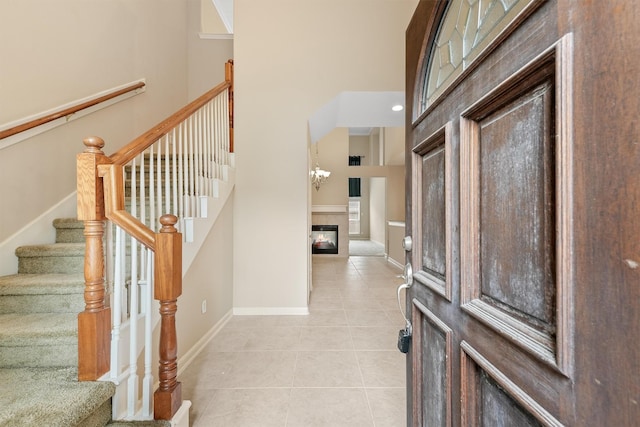 entryway with a glass covered fireplace, baseboards, a towering ceiling, and light tile patterned flooring