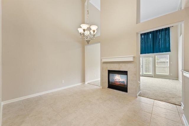 unfurnished living room featuring baseboards, a high ceiling, a chandelier, and a tile fireplace