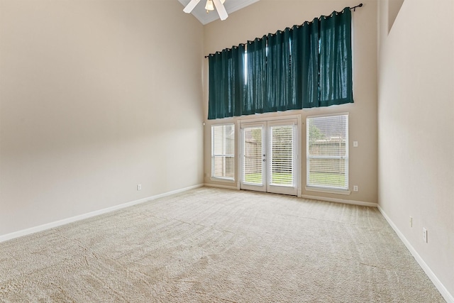 carpeted spare room featuring french doors, a ceiling fan, baseboards, and a towering ceiling