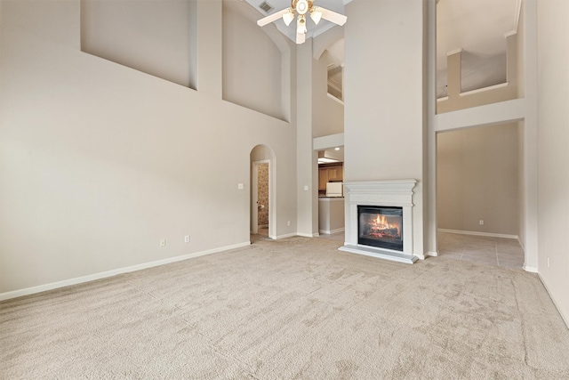 unfurnished living room with a ceiling fan, a glass covered fireplace, carpet, a high ceiling, and baseboards