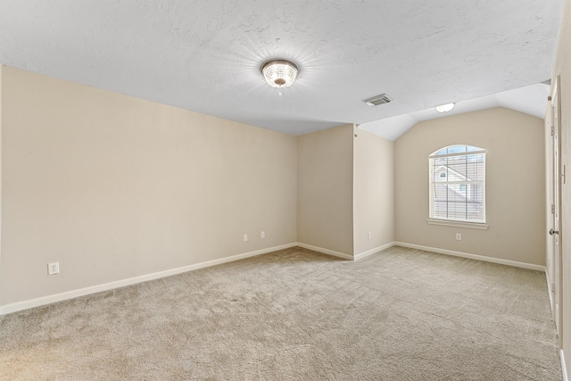 carpeted spare room featuring visible vents, a textured ceiling, baseboards, and lofted ceiling