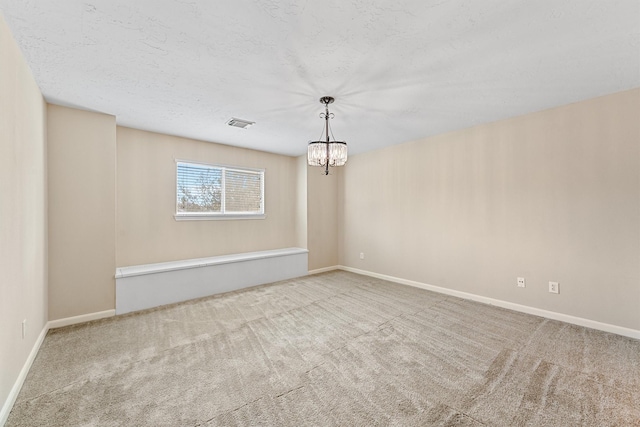 carpeted empty room featuring a notable chandelier, visible vents, baseboards, and a textured ceiling