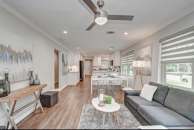 living area with visible vents, plenty of natural light, light wood-style flooring, and crown molding