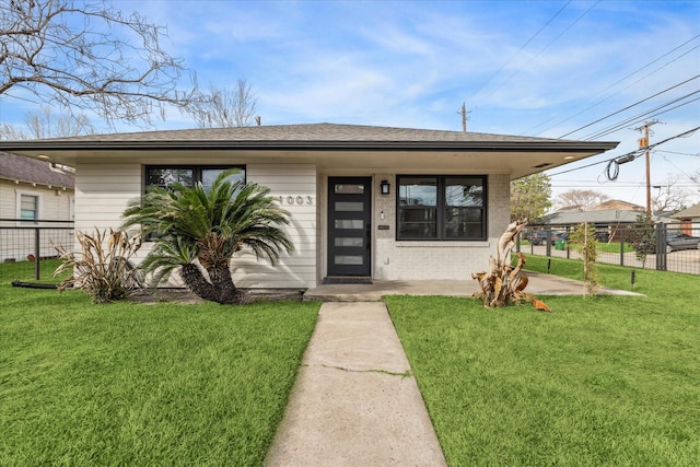 bungalow-style house featuring brick siding, a shingled roof, a front lawn, and fence