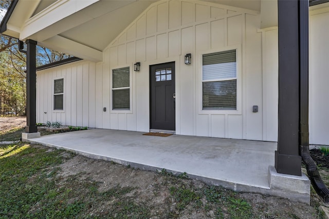 view of exterior entry with board and batten siding and a patio