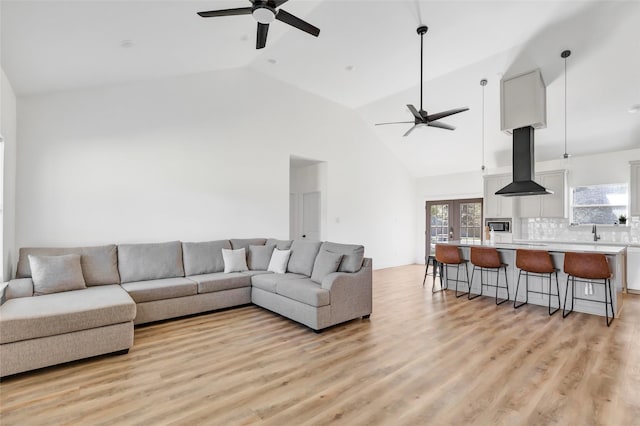 living room with high vaulted ceiling, french doors, light wood-style floors, and a ceiling fan