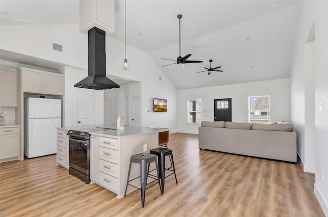 kitchen featuring visible vents, a kitchen breakfast bar, stainless steel electric stove, freestanding refrigerator, and exhaust hood