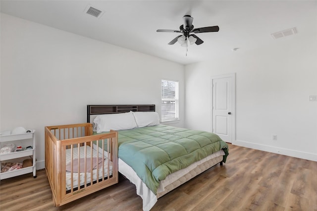 bedroom featuring visible vents, a ceiling fan, baseboards, and wood finished floors