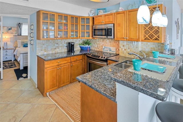 kitchen featuring brown cabinetry, dark stone countertops, stainless steel appliances, and a sink