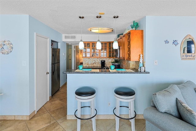 kitchen featuring visible vents, appliances with stainless steel finishes, a peninsula, brown cabinetry, and glass insert cabinets