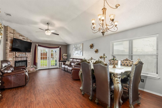 dining space with wood finished floors, lofted ceiling, a textured ceiling, a brick fireplace, and ceiling fan with notable chandelier