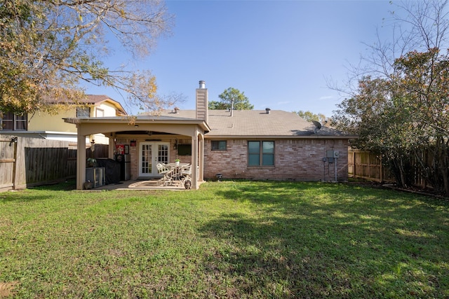 rear view of house with brick siding, french doors, a fenced backyard, and a chimney
