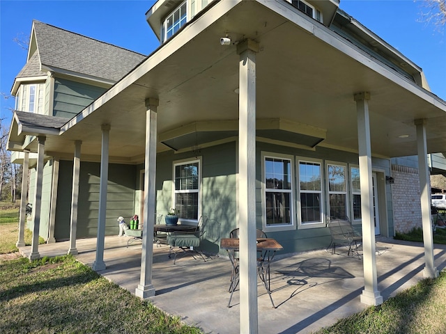 rear view of house with covered porch, a shingled roof, and a patio