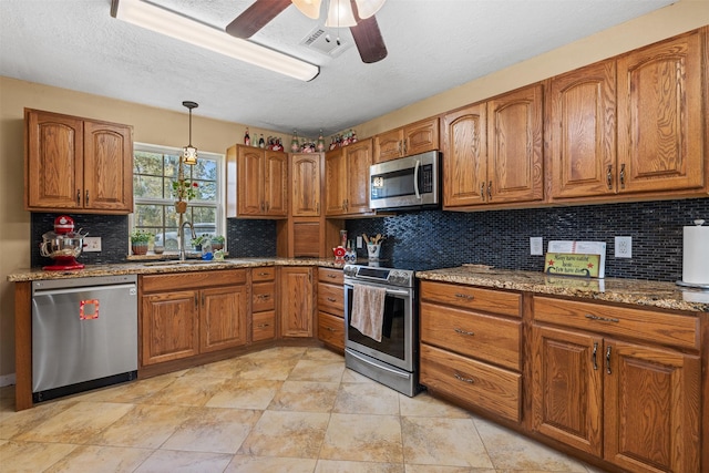 kitchen with visible vents, stone counters, appliances with stainless steel finishes, brown cabinetry, and a sink