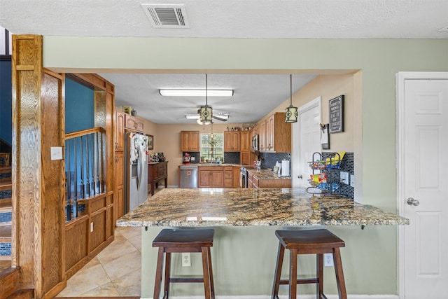 kitchen featuring light tile patterned floors, brown cabinetry, visible vents, a peninsula, and appliances with stainless steel finishes