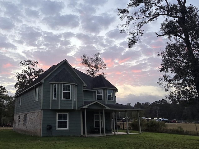 back of house at dusk with a lawn, brick siding, and a patio area