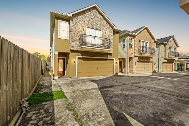 townhome / multi-family property featuring stucco siding, driveway, fence, a garage, and a balcony