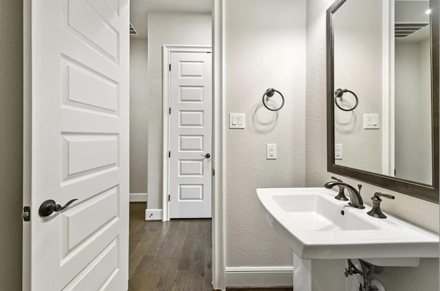 bathroom featuring wood finished floors, baseboards, a textured wall, and a sink