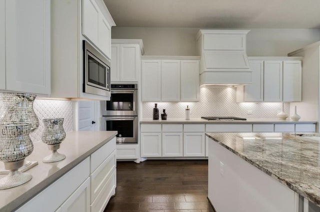 kitchen with tasteful backsplash, appliances with stainless steel finishes, white cabinets, and dark wood finished floors