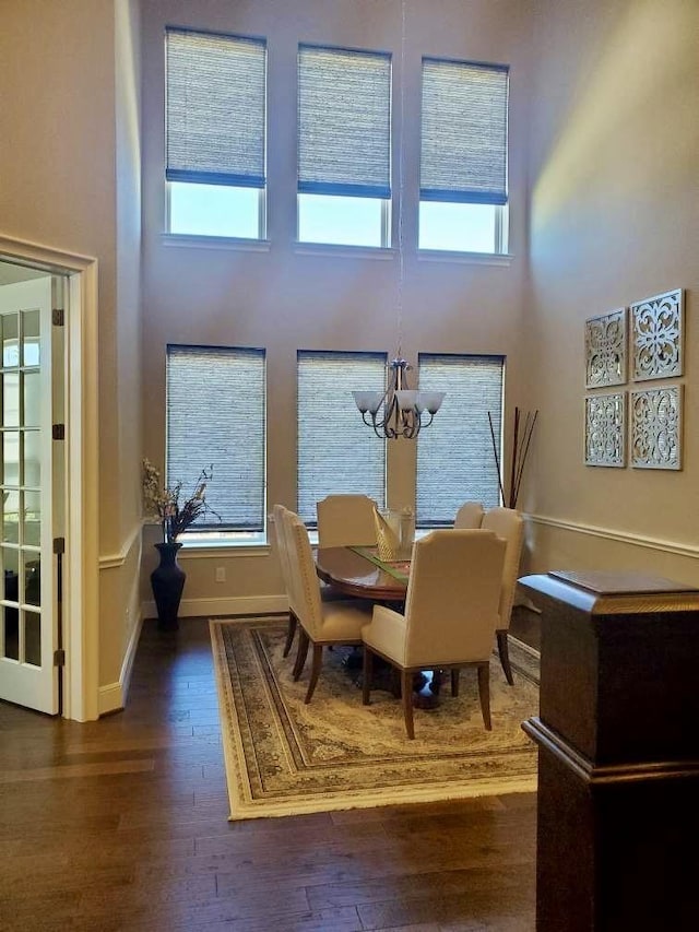 dining room featuring baseboards, dark wood-style flooring, a towering ceiling, and a chandelier