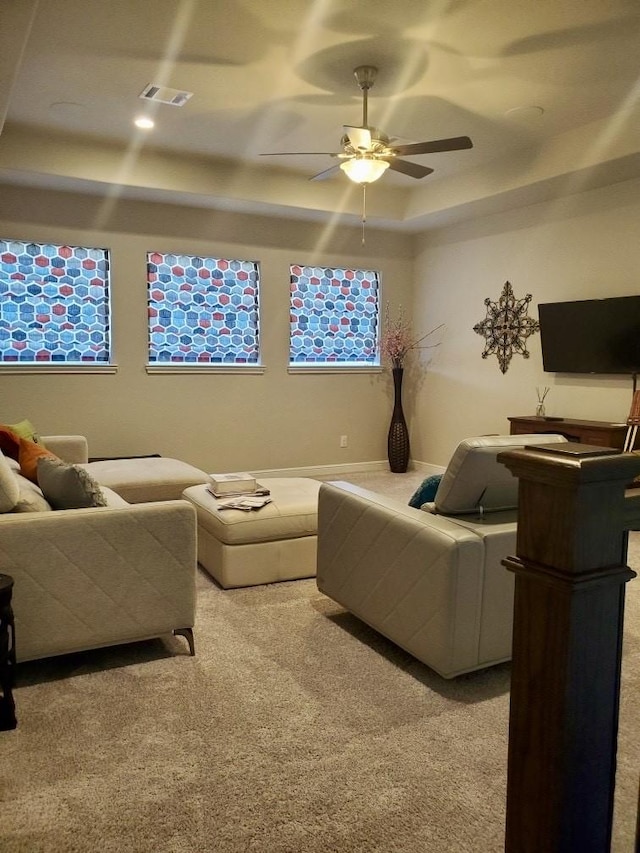 living area with carpet, visible vents, plenty of natural light, ceiling fan, and a raised ceiling