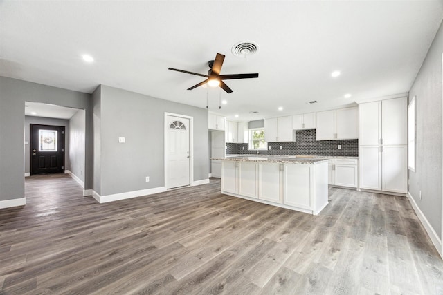 kitchen featuring light wood finished floors, visible vents, a kitchen island, decorative backsplash, and white cabinetry