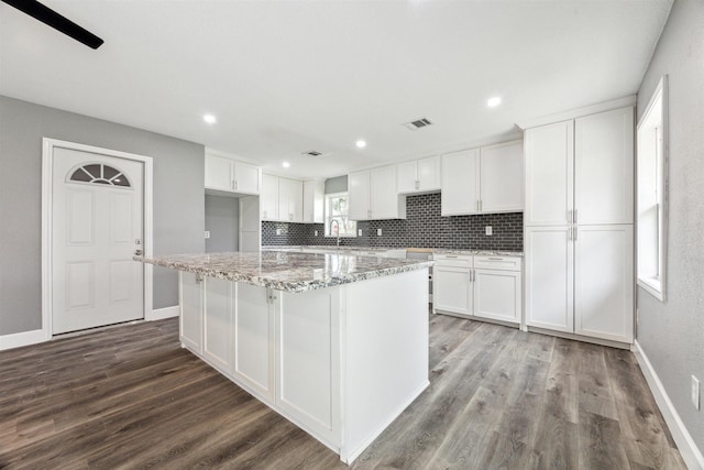 kitchen with white cabinets, light stone counters, wood finished floors, and tasteful backsplash