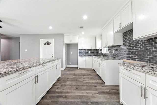 kitchen with dark wood finished floors, white cabinets, light stone countertops, and backsplash