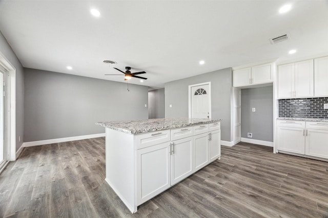 kitchen with visible vents, a kitchen island, dark wood-type flooring, white cabinetry, and backsplash