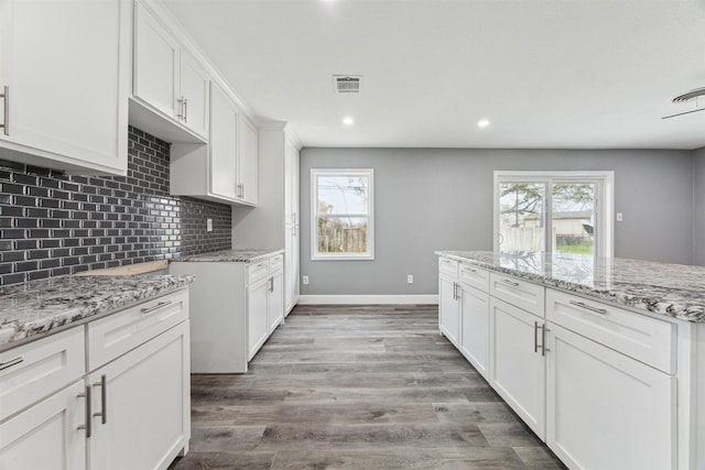 kitchen featuring light stone counters, baseboards, visible vents, light wood finished floors, and tasteful backsplash