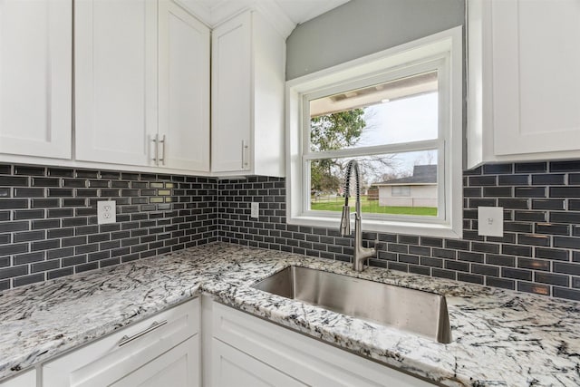 kitchen featuring tasteful backsplash, white cabinets, light stone countertops, and a sink