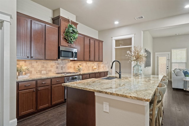 kitchen with dark wood-type flooring, a sink, light stone counters, backsplash, and appliances with stainless steel finishes