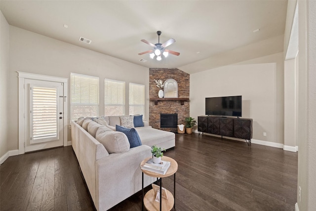 living area with visible vents, a ceiling fan, a fireplace, dark wood-style flooring, and vaulted ceiling