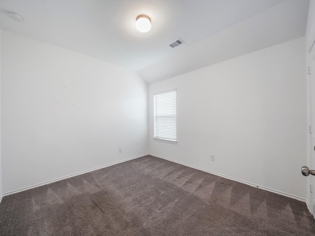 spare room featuring visible vents, lofted ceiling, baseboards, and dark carpet