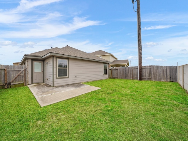 rear view of house featuring a patio, a lawn, roof with shingles, and a fenced backyard