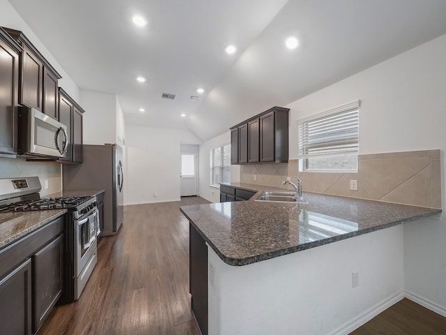 kitchen featuring dark brown cabinetry, appliances with stainless steel finishes, dark stone counters, and a sink