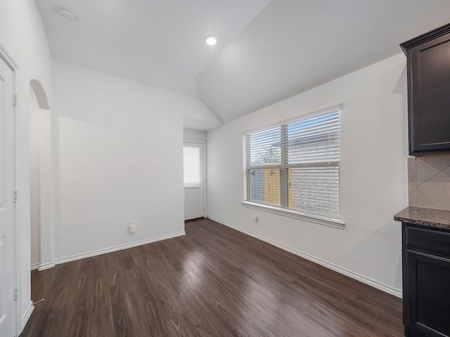 interior space featuring baseboards, arched walkways, dark wood-style flooring, and vaulted ceiling