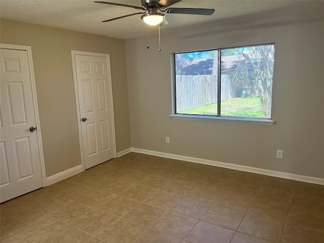 unfurnished bedroom featuring light tile patterned floors, a textured ceiling, baseboards, and a ceiling fan