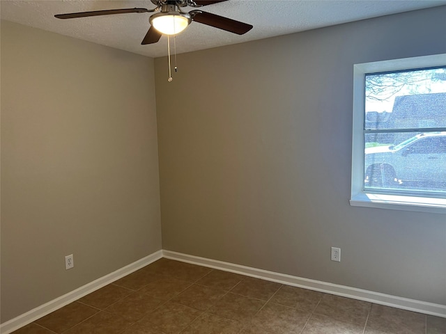 unfurnished room featuring dark tile patterned flooring, a ceiling fan, baseboards, and a textured ceiling