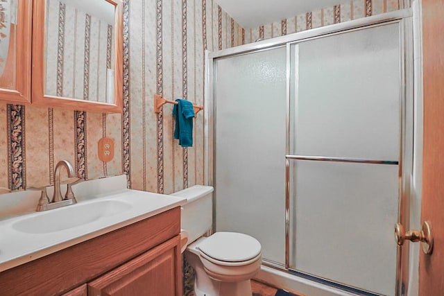 bathroom with a shower stall, wallpapered walls, vanity, and toilet