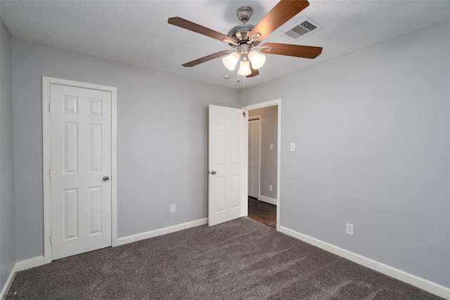 unfurnished bedroom featuring visible vents, baseboards, a textured ceiling, a ceiling fan, and dark colored carpet