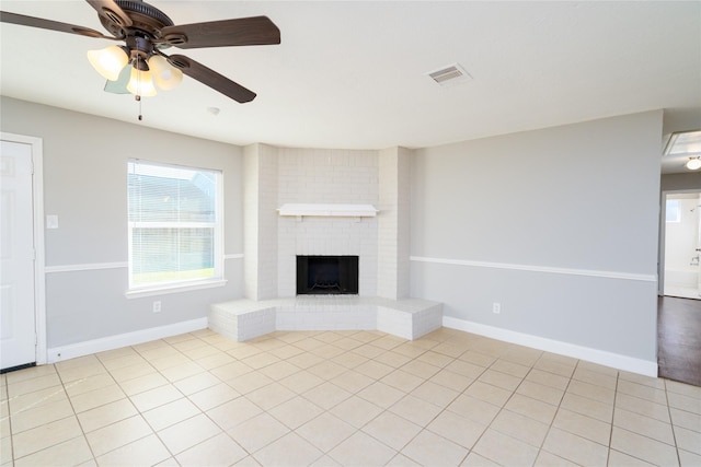 unfurnished living room with a brick fireplace, baseboards, visible vents, and ceiling fan