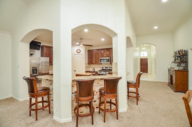 kitchen featuring light colored carpet, appliances with stainless steel finishes, a kitchen breakfast bar, and ornamental molding