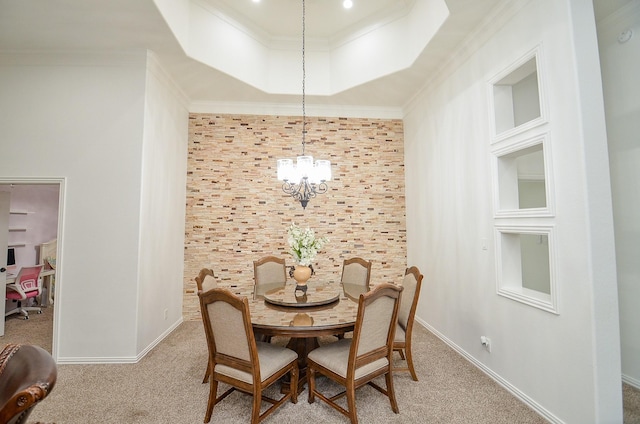 carpeted dining area with a tray ceiling, an inviting chandelier, crown molding, baseboards, and an accent wall