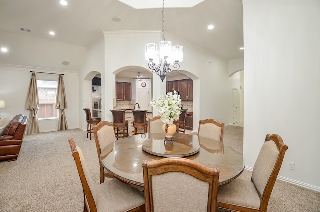 dining area with arched walkways, light colored carpet, a chandelier, and crown molding