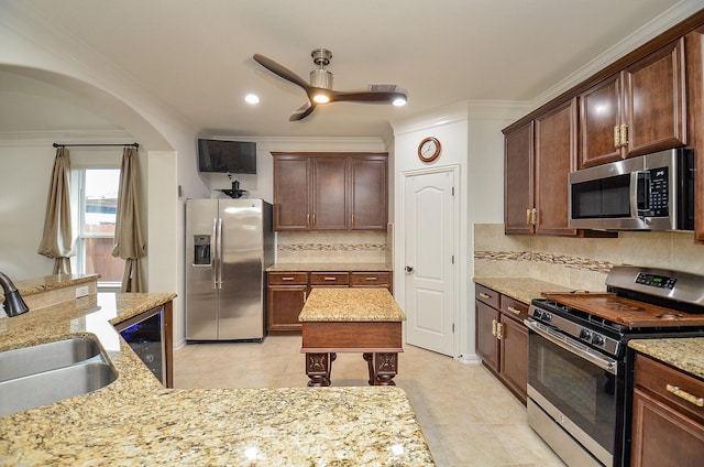 kitchen with a kitchen island, crown molding, light stone counters, stainless steel appliances, and a sink