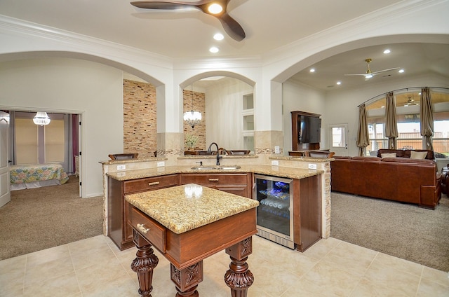 kitchen with light stone counters, beverage cooler, ceiling fan, light colored carpet, and open floor plan