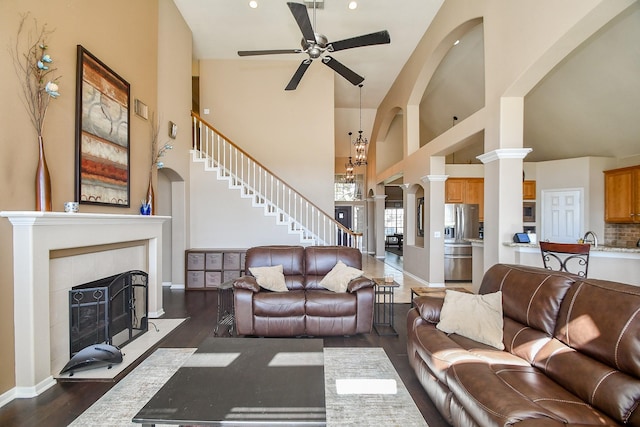 living area featuring a ceiling fan, decorative columns, a fireplace, a high ceiling, and dark wood-type flooring